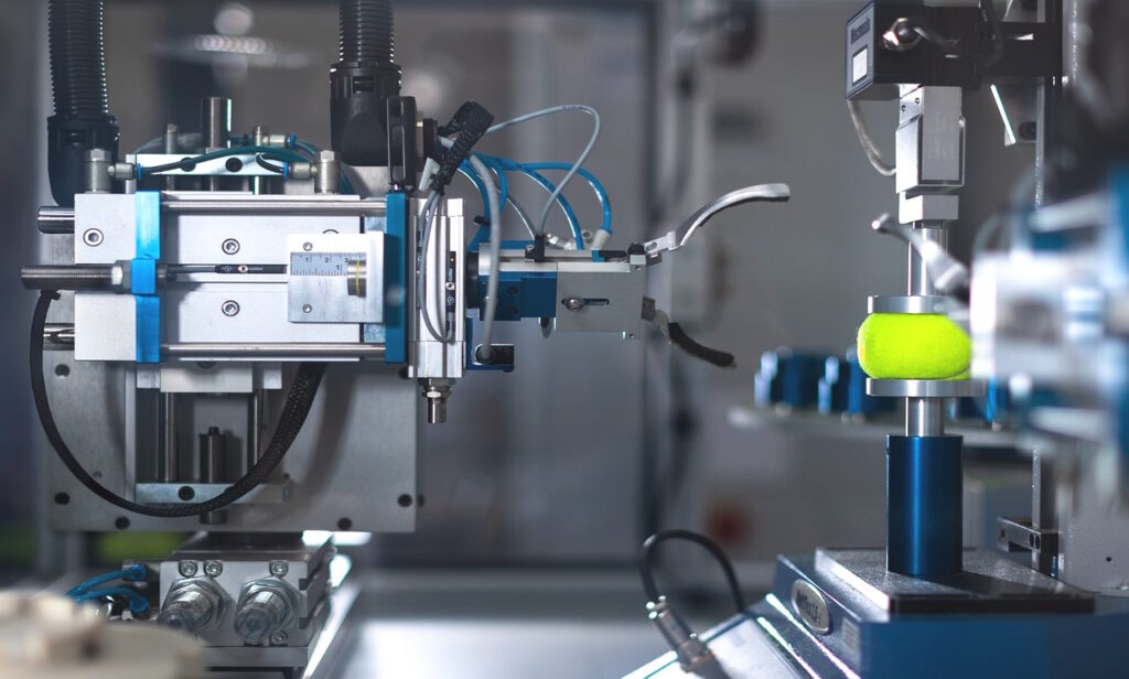 Close-up image of a robotic automation system in a precision manufacturing facility testing the compression or resilience of a fluorescent yellow tennis ball