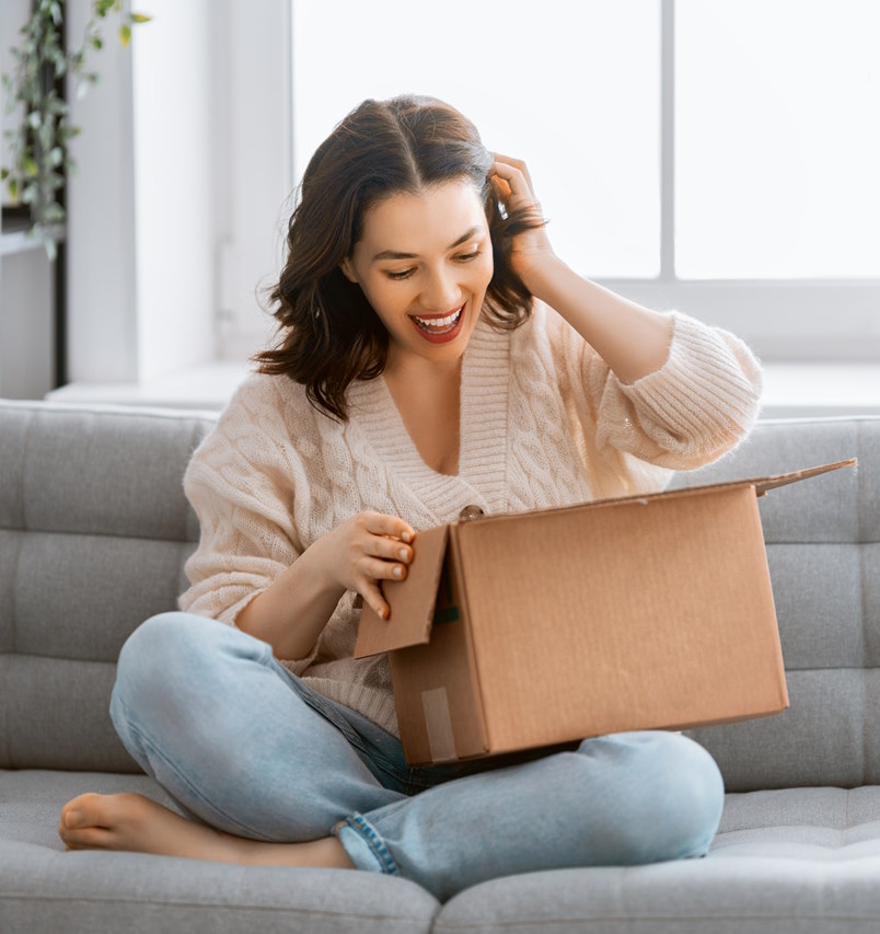 A joyful woman sitting on a couch, excitedly unboxing a package